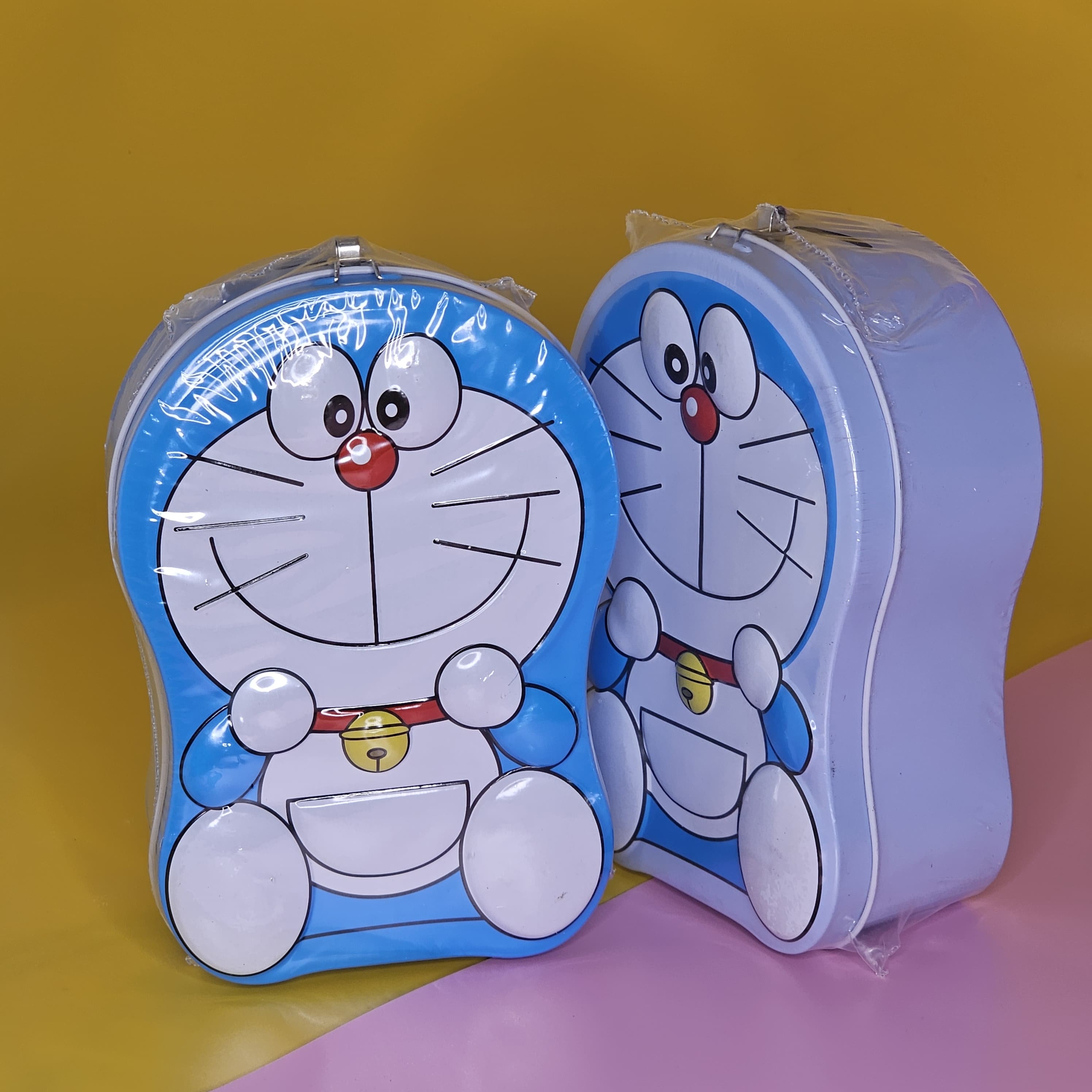Blue and white Doraemon-shaped metal money box (piggy bank) with a top slot for coins, featuring a lock and key for secure saving. Ideal gift for kids from uSmile.toys." www.usmile.toys